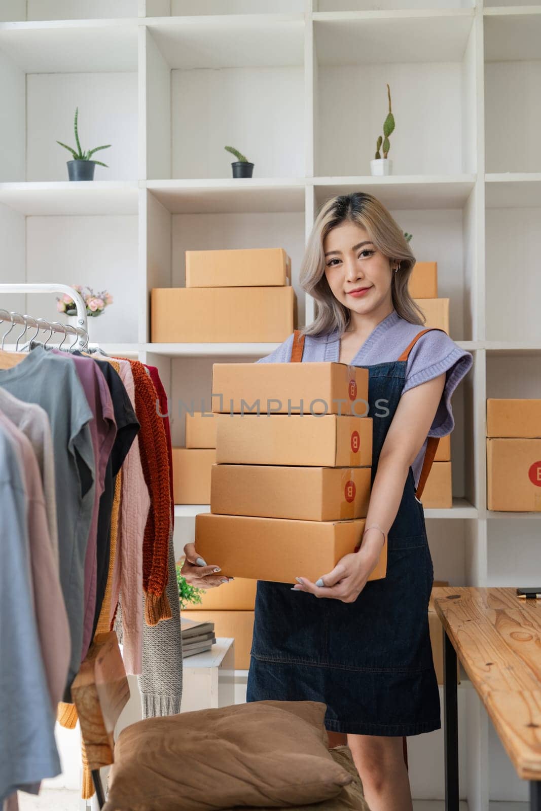 Portrait of Asian woman sell clothing online and looking at camera. Attractive beautiful young business woman standing hold the box confident in house by nateemee