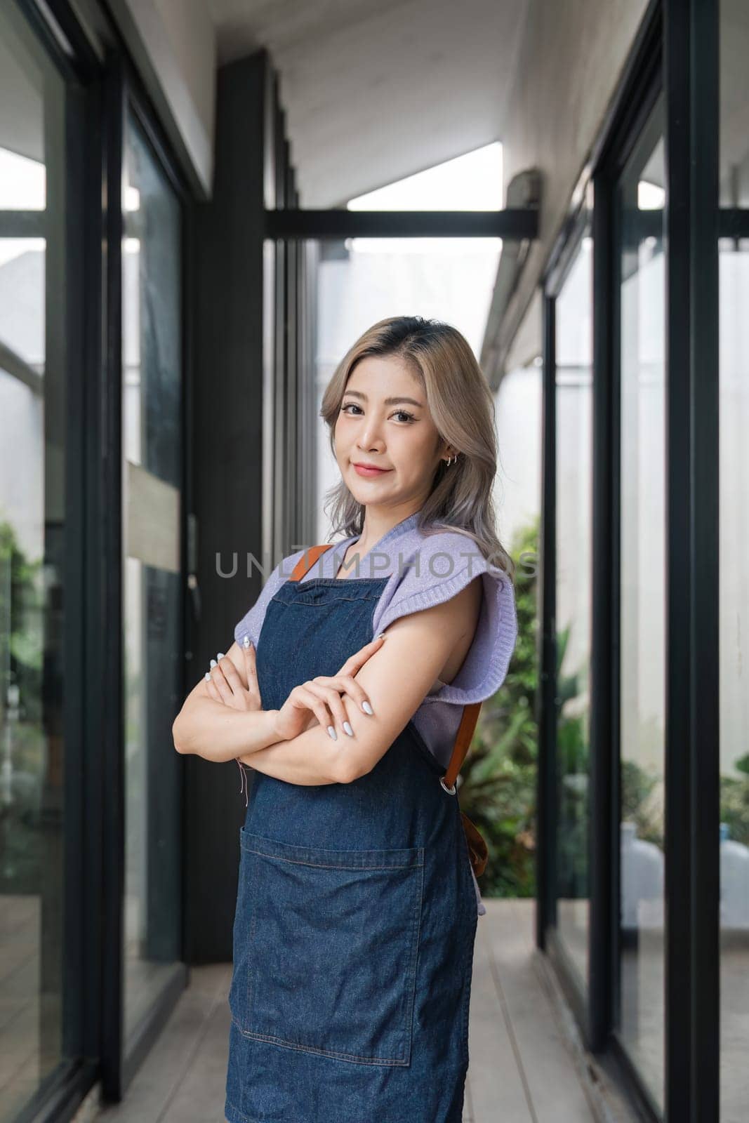 Young asian businesswoman small business owner standing at door entrance , A cheerful entrepreneur young waitress in a blue apron near the glass door by nateemee