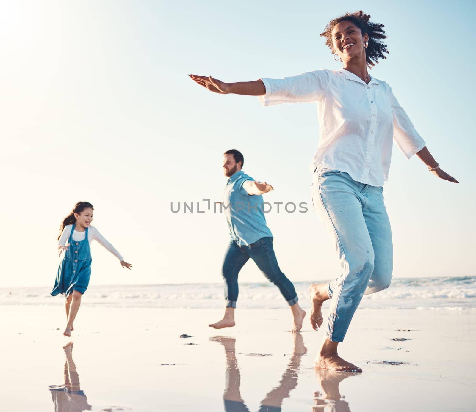 Mother, father and daughter on the beach to dance together while outdoor for travel or vacation in summer. Sunset, family or children and a girl having fun with her parents on the coast by the ocean by YuriArcurs