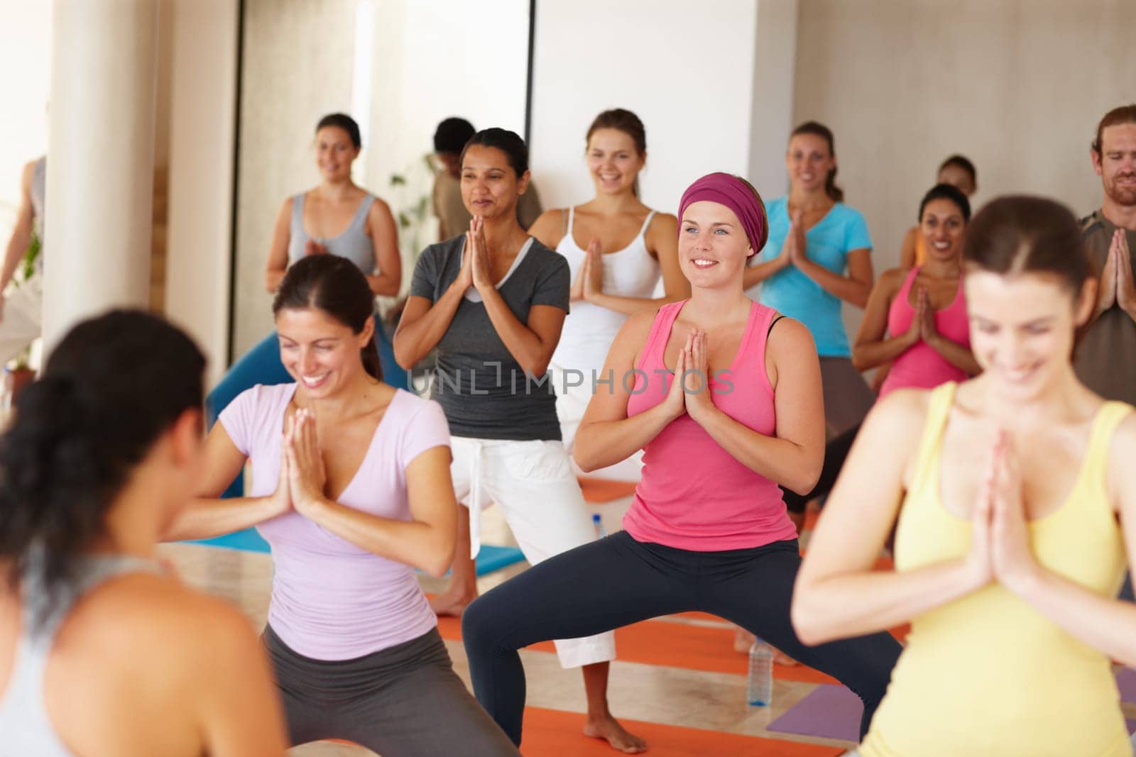 Enjoying their yoga workout. Shot of a group of smiling yoga students standing in front of their teacher and following her movements