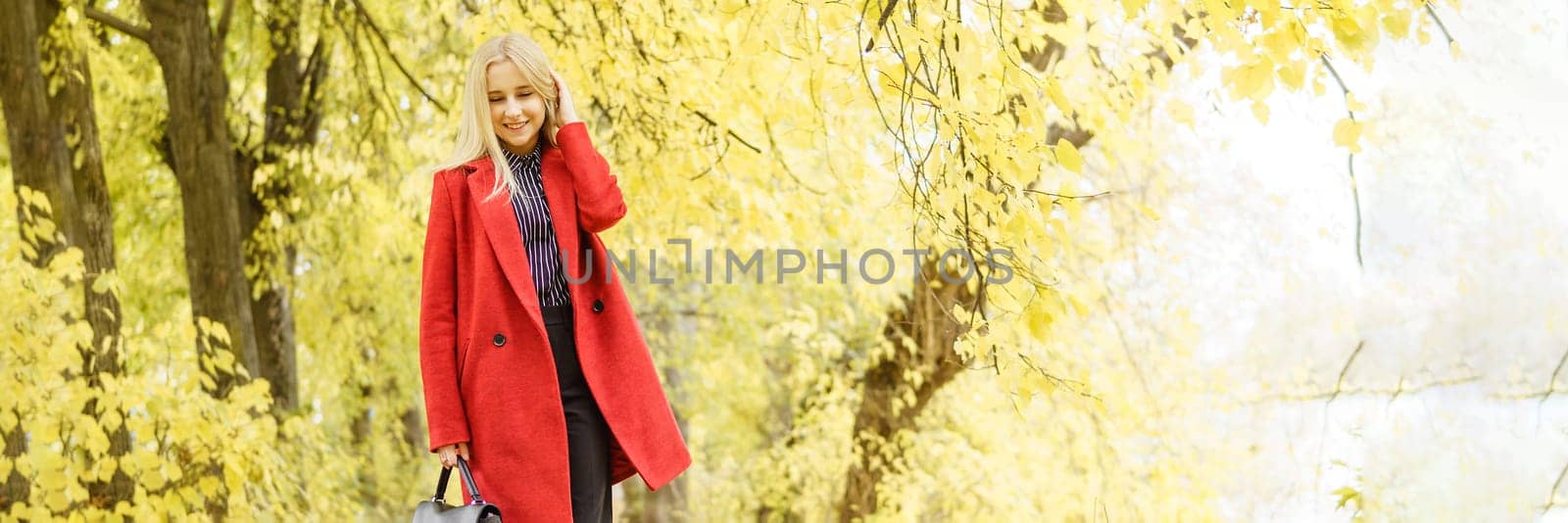 A young blonde woman walks around the autumn city in a red coat. The concept of urban style and lifestyle.