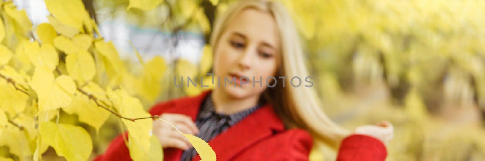 A young blonde woman walks around the autumn city in a red coat. The concept of urban style and lifestyle.