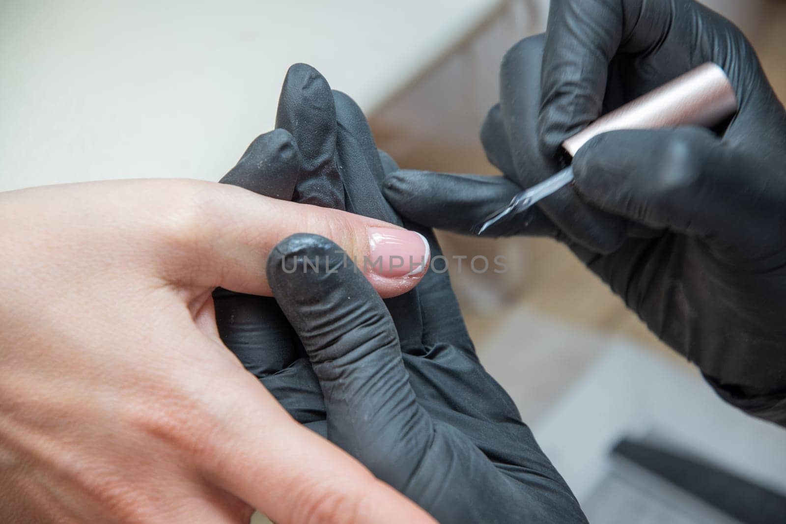 a master does a manicure to a client in a beauty salon and covers her nails with pink varnish. High quality photo