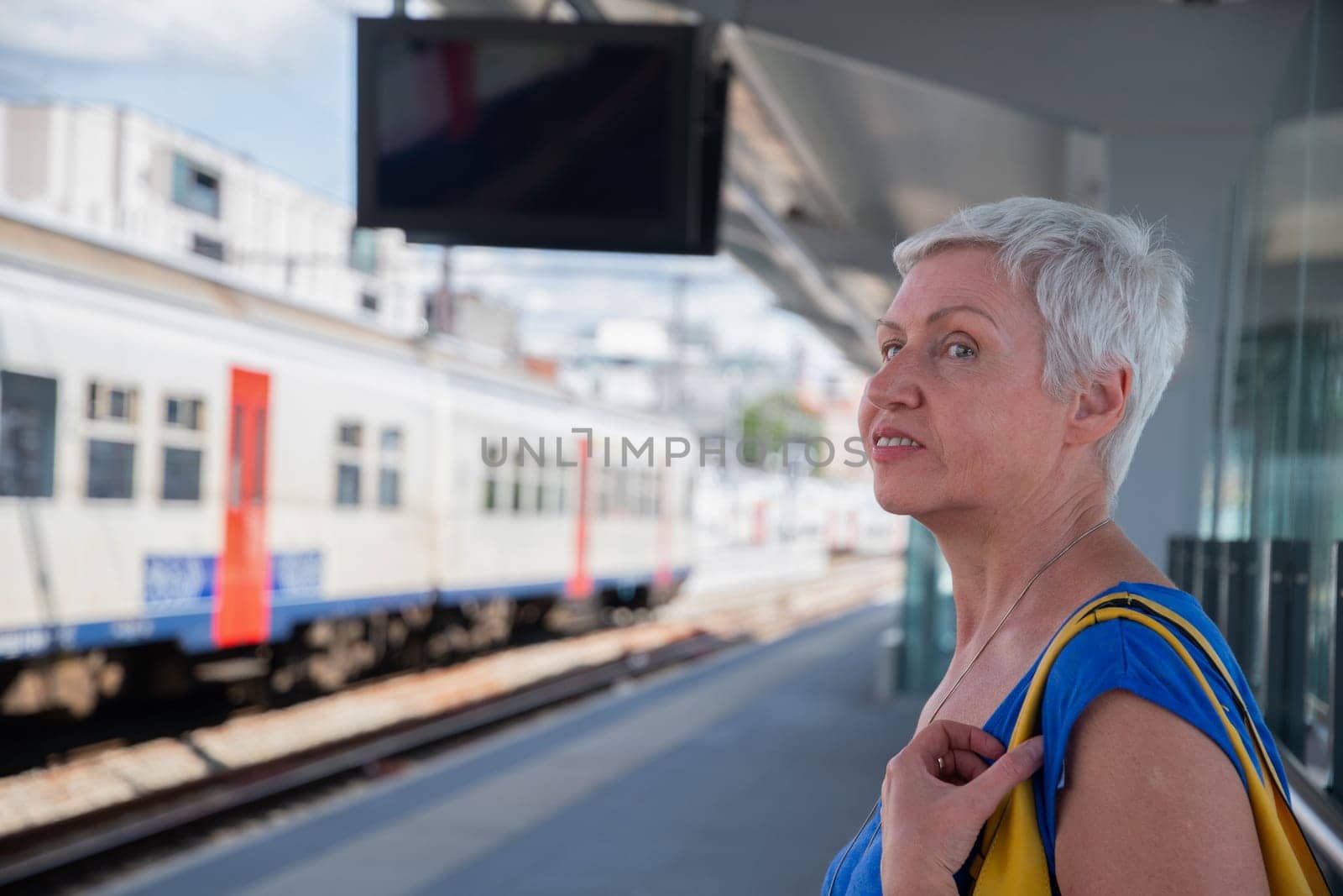 Active gray-haired woman waiting for a train on the platform of the city station, travel, tourism, public transport, Middle-aged woman leading a healthy lifestyle, High Quality Photo