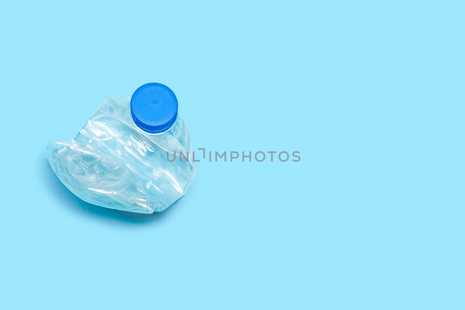 Flat plastic bottle recycling design blue background. One used bottle PET plastic recycling concept. Single crushed bottle crumpled plastic garbage PET recycling background top view