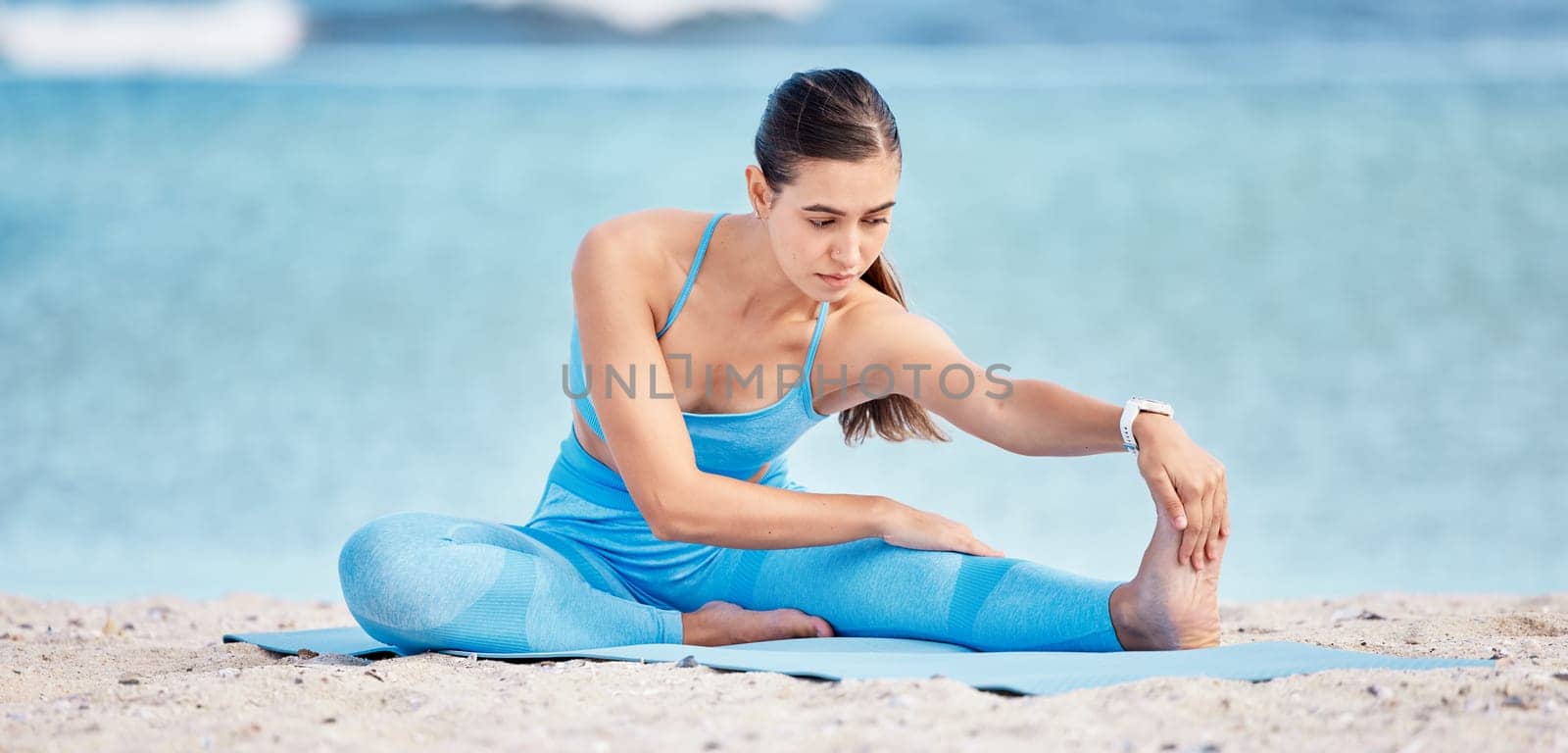 Stretching legs, yoga and woman by beach on sports mat for wellness, healthy body and balance. Performance, nature and female person outdoors for exercise, training and workout by sea for pilates.