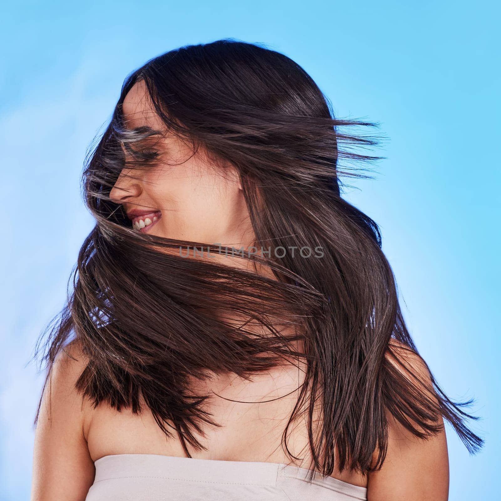 Woman, shake hair and beauty with shine, volume and texture against a blue studio background. Growth, person and model satisfied with salon treatment, glow and change with self care, playful and fun.