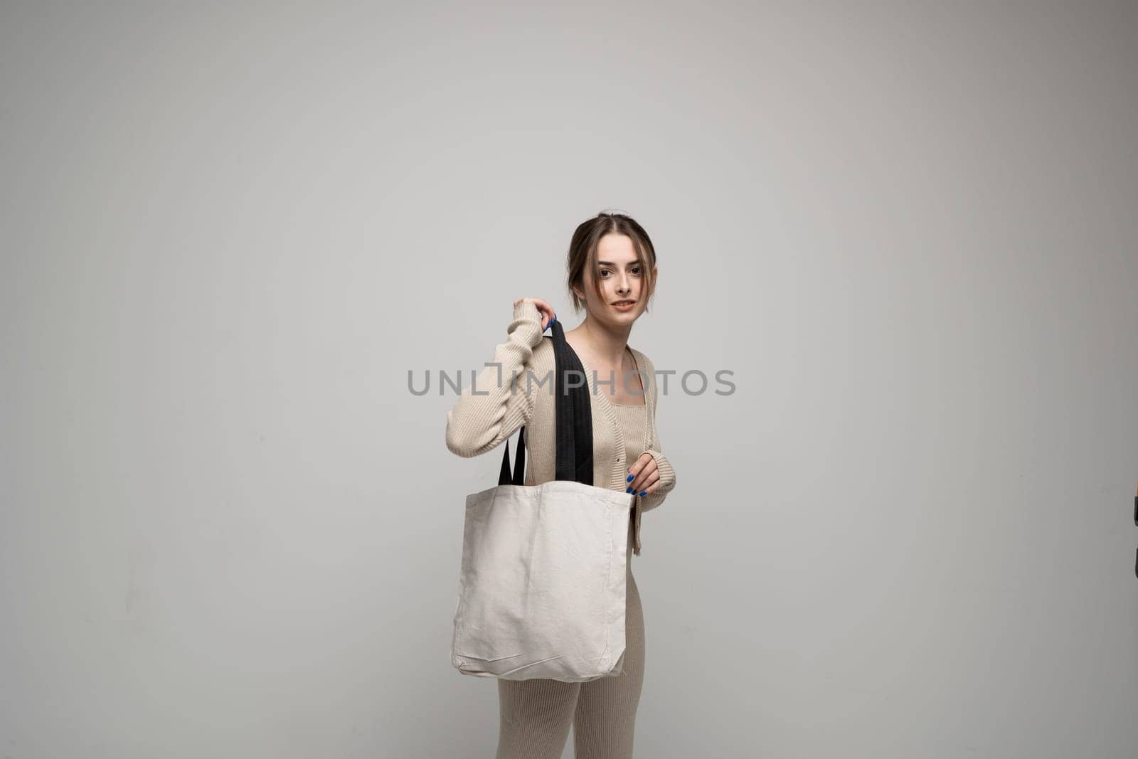 Cheerful millennial woman with a white eco bag standing over white studio background. Lady holding shopper handbag. Fashion and ecology concept, Selective Focus. No more plastic
