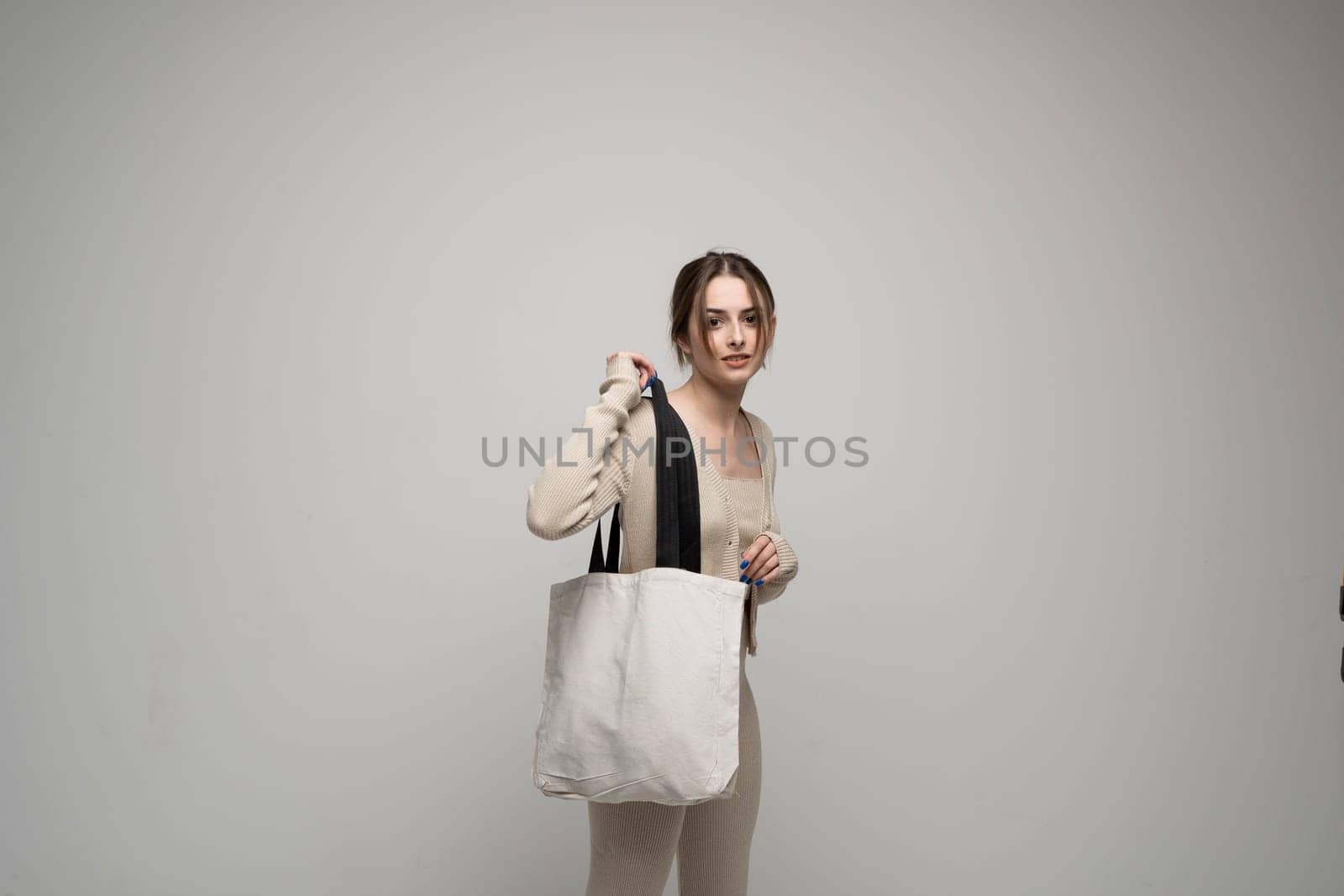 Cheerful millennial woman with a white eco bag standing over white studio background. Lady holding shopper handbag. Fashion and ecology concept, Selective Focus. No more plastic. by vovsht