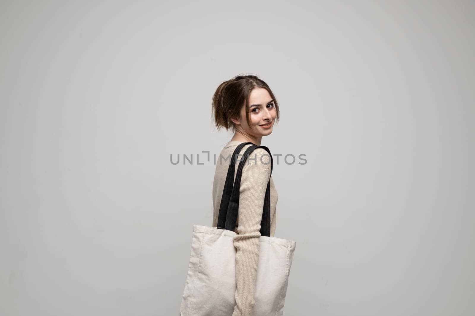 Happy, smiling brunette young woman carrying reusable cotton bag. Concept of recycle for better environment. No plastic. by vovsht