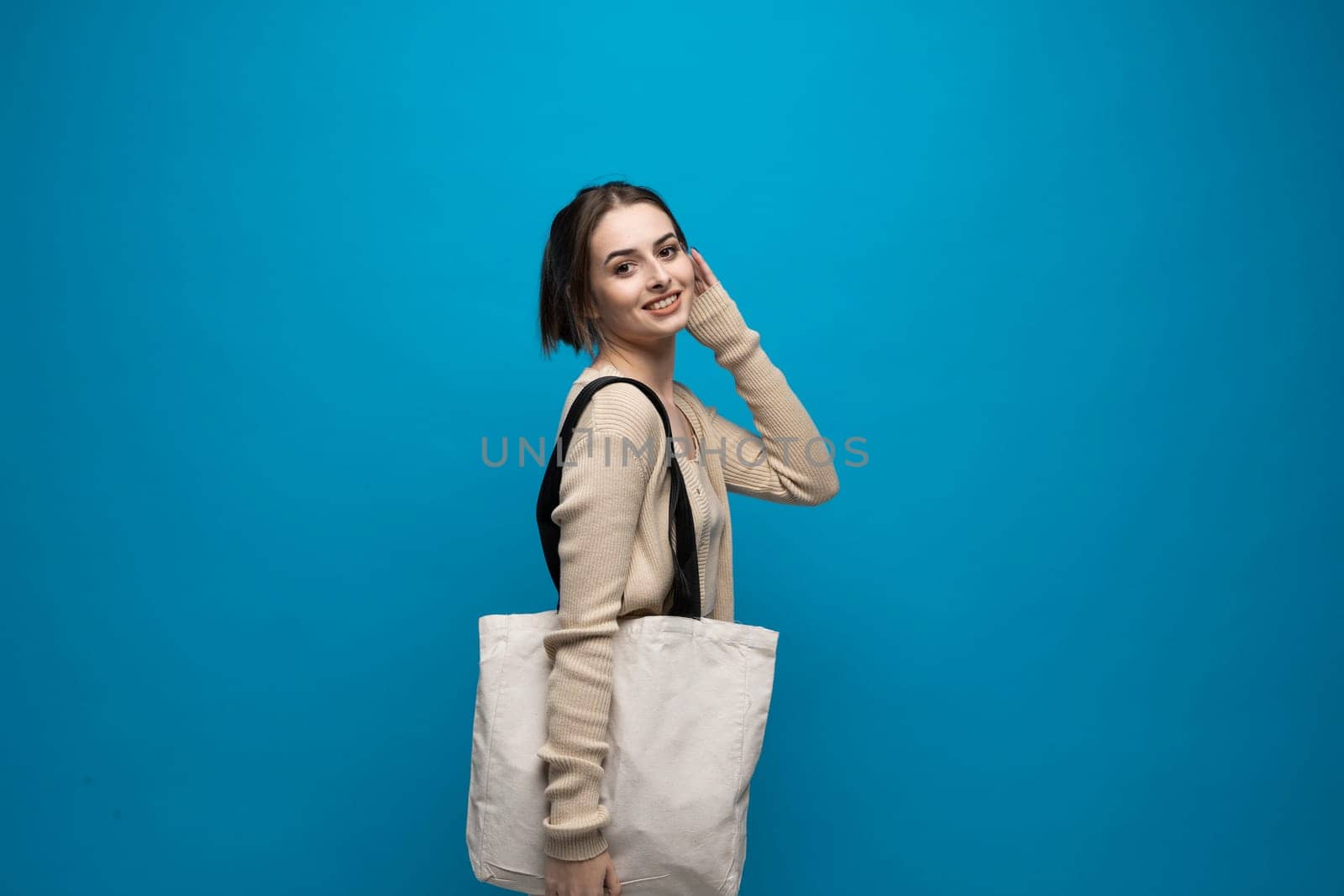 Brunette cheerful millennial woman holding white eco bag standing over white studio background. Concept of recycle for better environment. No plastic. Fashion and ecology concept