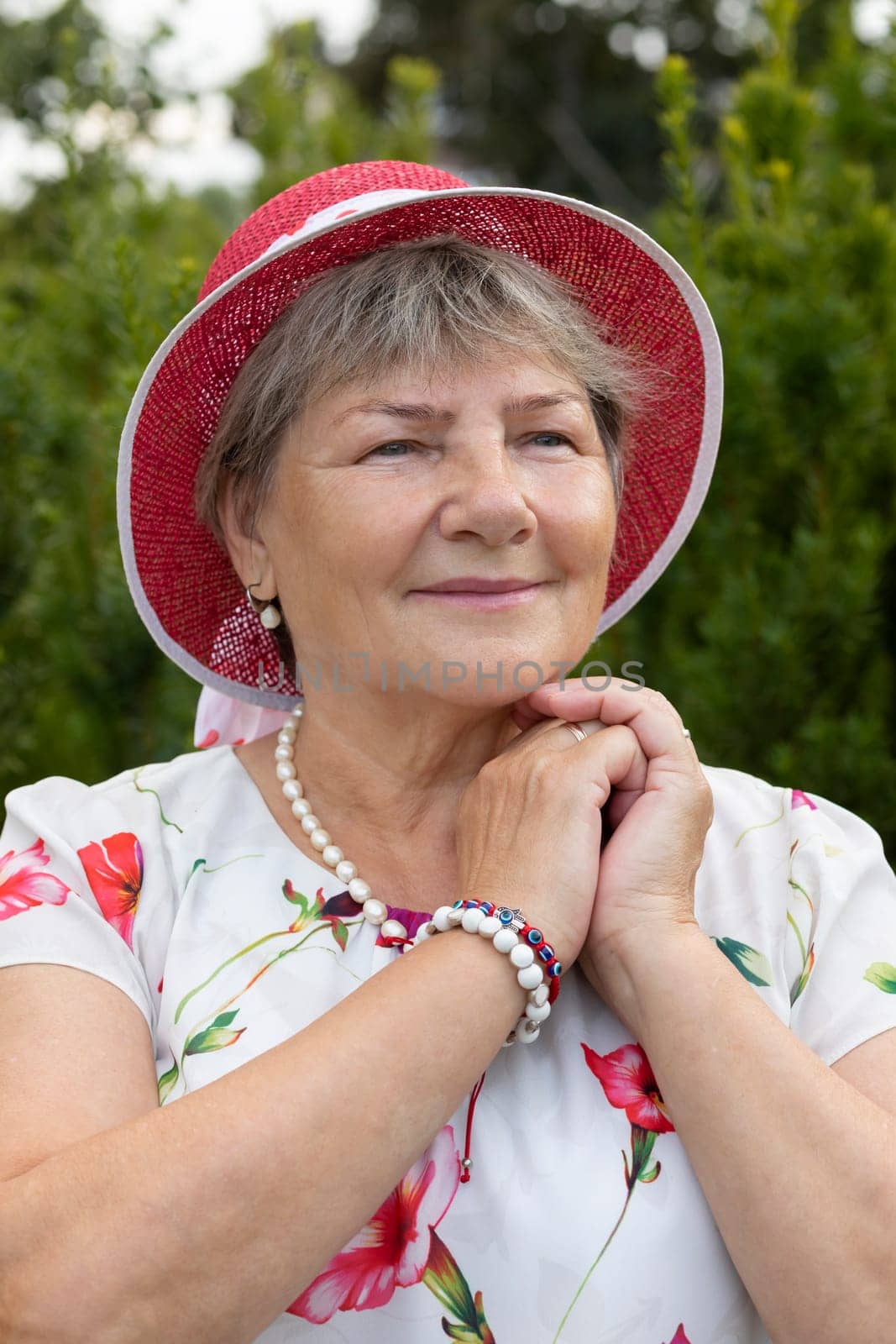 Portrait Real Happy Smiling Senior Woman In Hat. Green Trees, Park on Background. Pleased Elderly 70s Carefree, Full of Hope Beautiful Granny Looking Away Vertical Plane. High quality photo