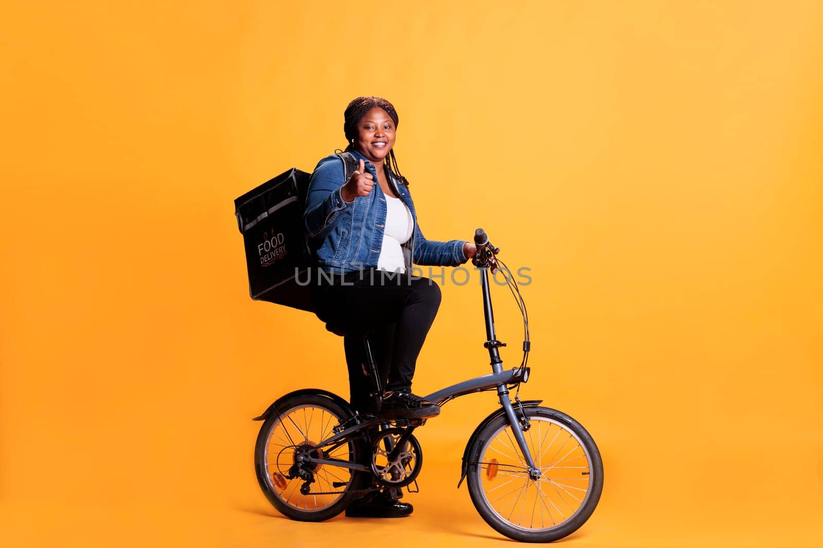 Pizzeria delivery worker doing thumbs up gesture while holding pizza cardboard, delivering take away food meal to customer. Courier bringing lunch order with bike as transportation