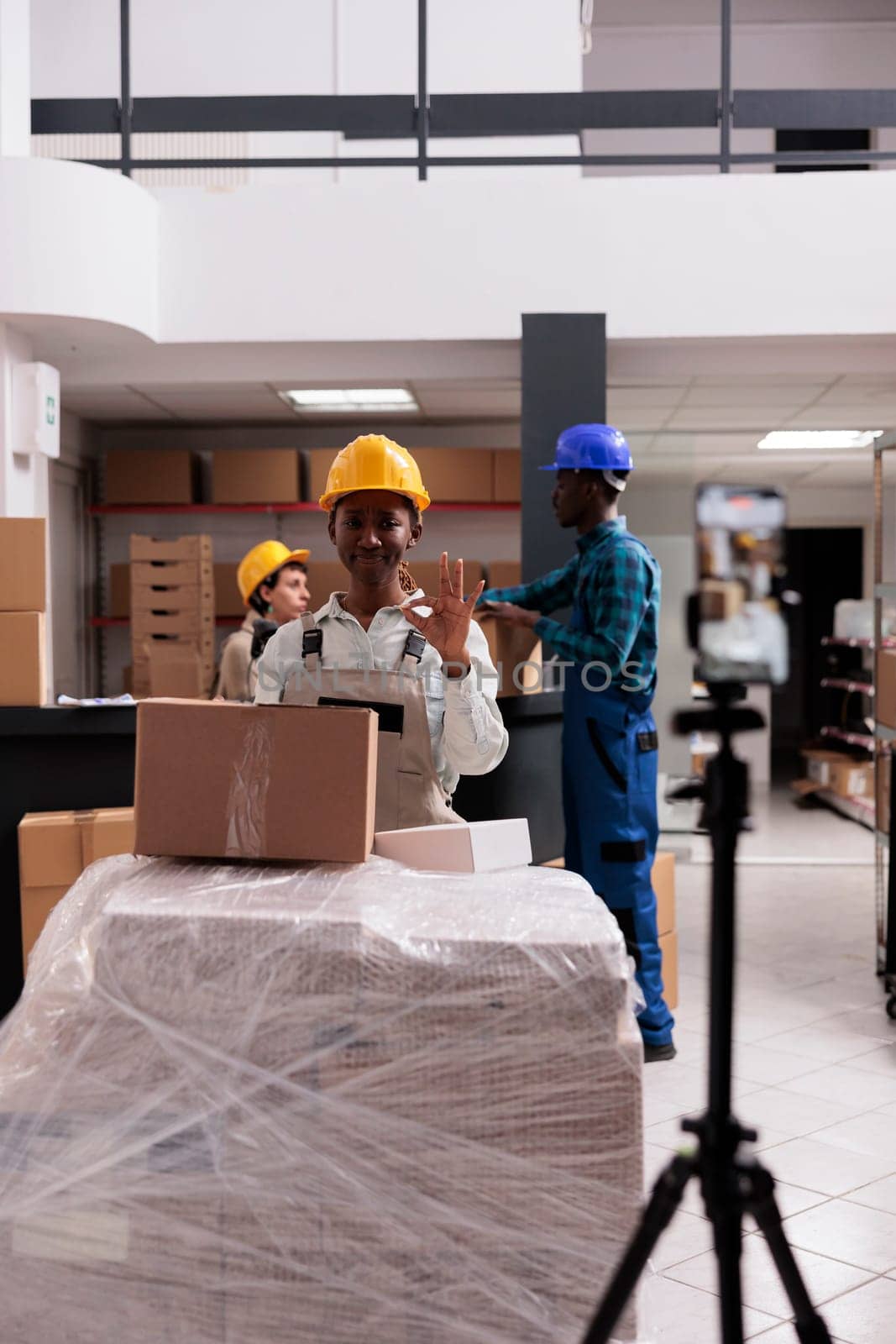 Storehouse employee shooting stock checking video and showing ok gesture with fingers. Retail storehouse workers doing goods inventory and looking at mobile phone camera with okay sign