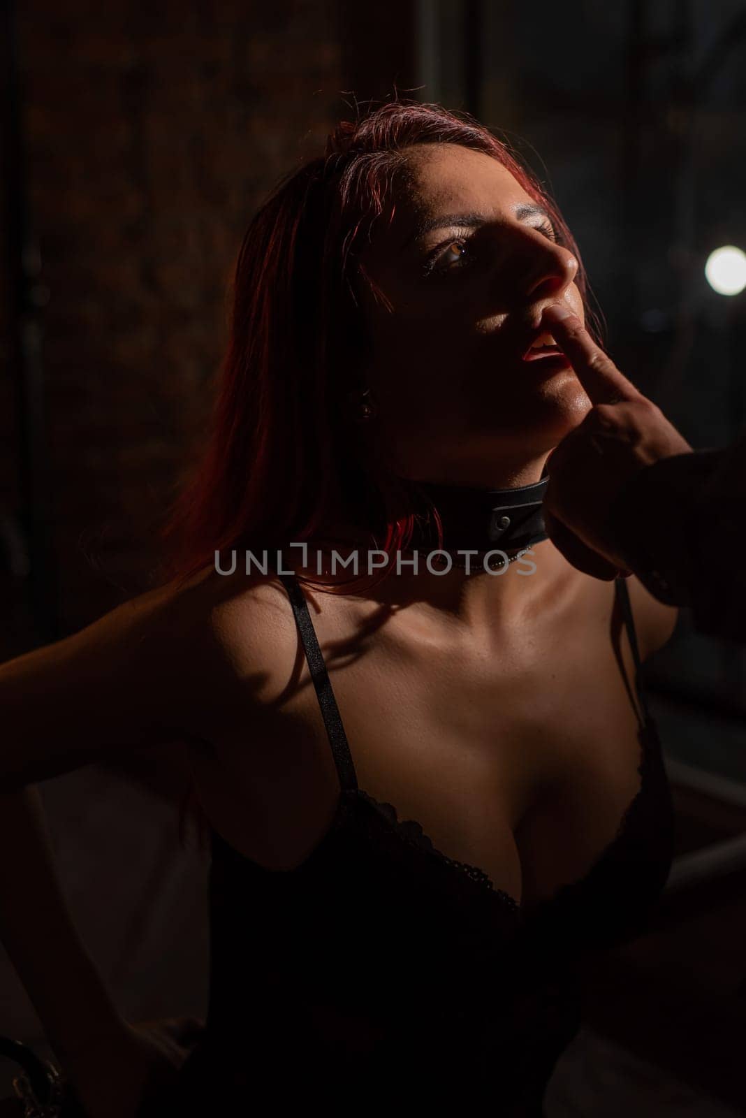 BDSM. Portrait of a red-haired woman in shackles kneeling and licking the fingers of a man. by mrwed54