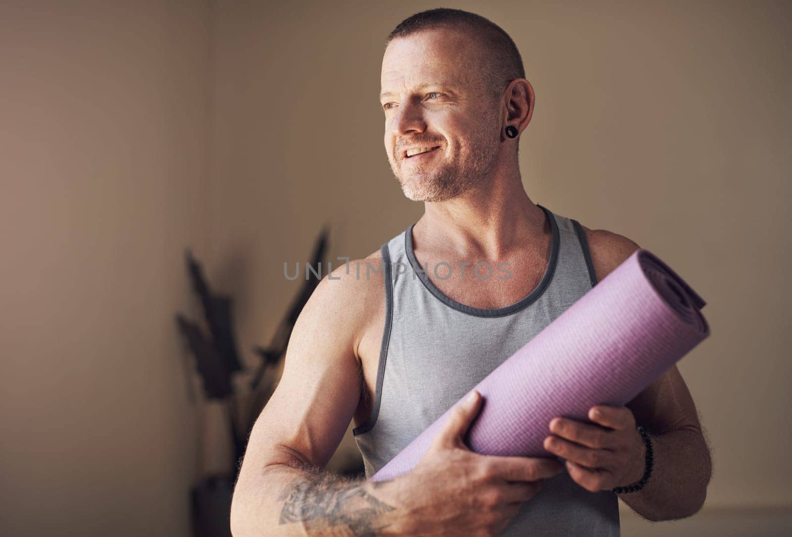 Yoga helps me slow down and appreciate life. Cropped shot of a handsome young man standing alone and holding his yoga mat before an indoor yoga session. by YuriArcurs