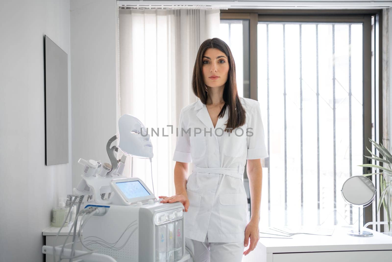 Woman cosmetologist standing and looking at camera in beauty spa salon. Female dermatologist, skin therapist, beautician skincare professional in clean white coat uniform