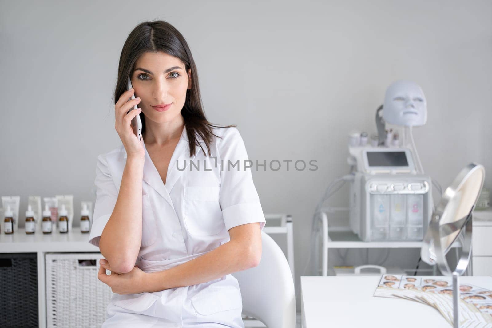 Beautician in cosmetology office have phone conversation. Dermatologist standing in beauty clinic discussing facial skin treatments for clients at beauty spa salon.