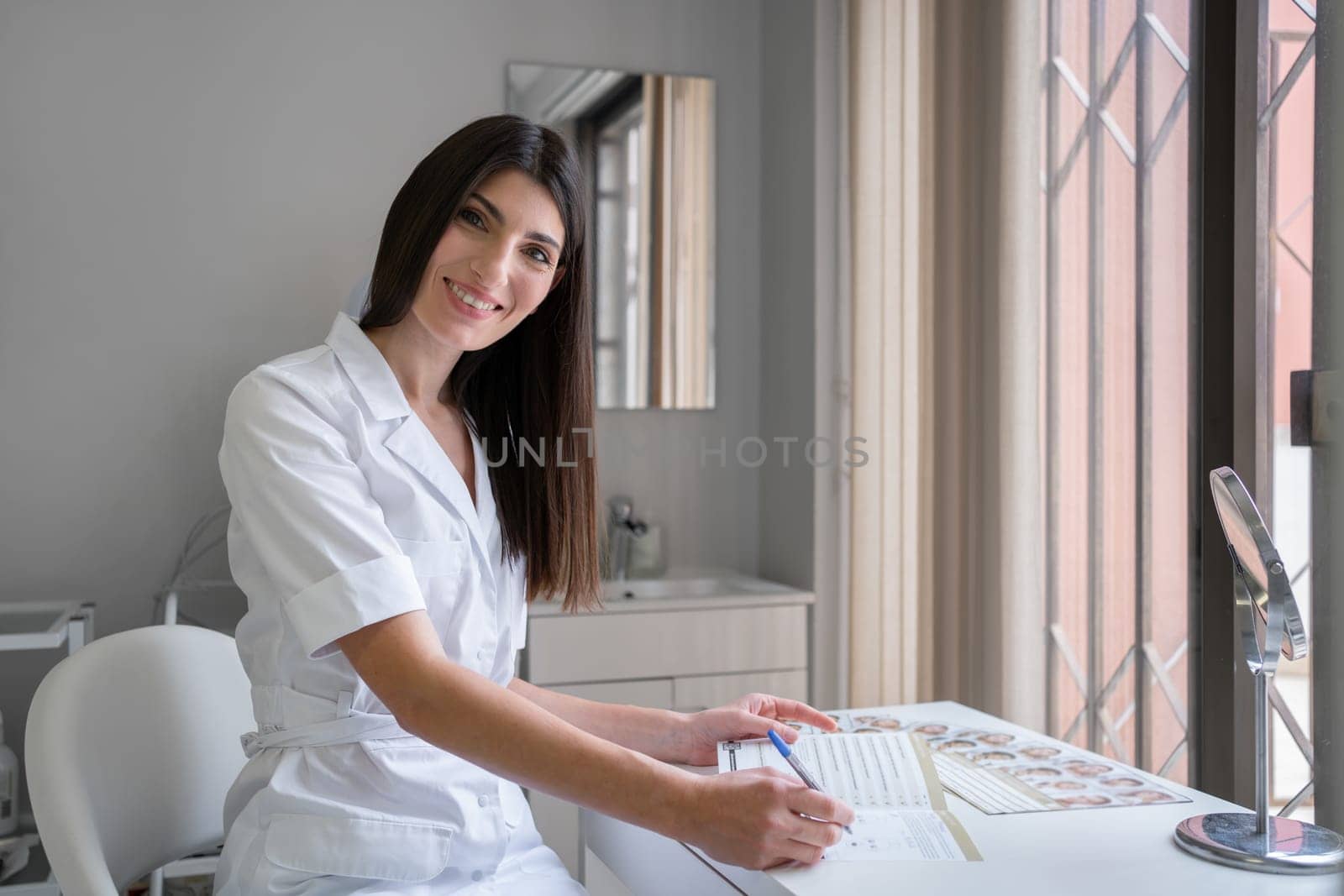 Female doctor in white coat filling out paper medical histories at her workplace. Carefully checking medical exams, writing notes, preparing documents, reports, and prescriptions.