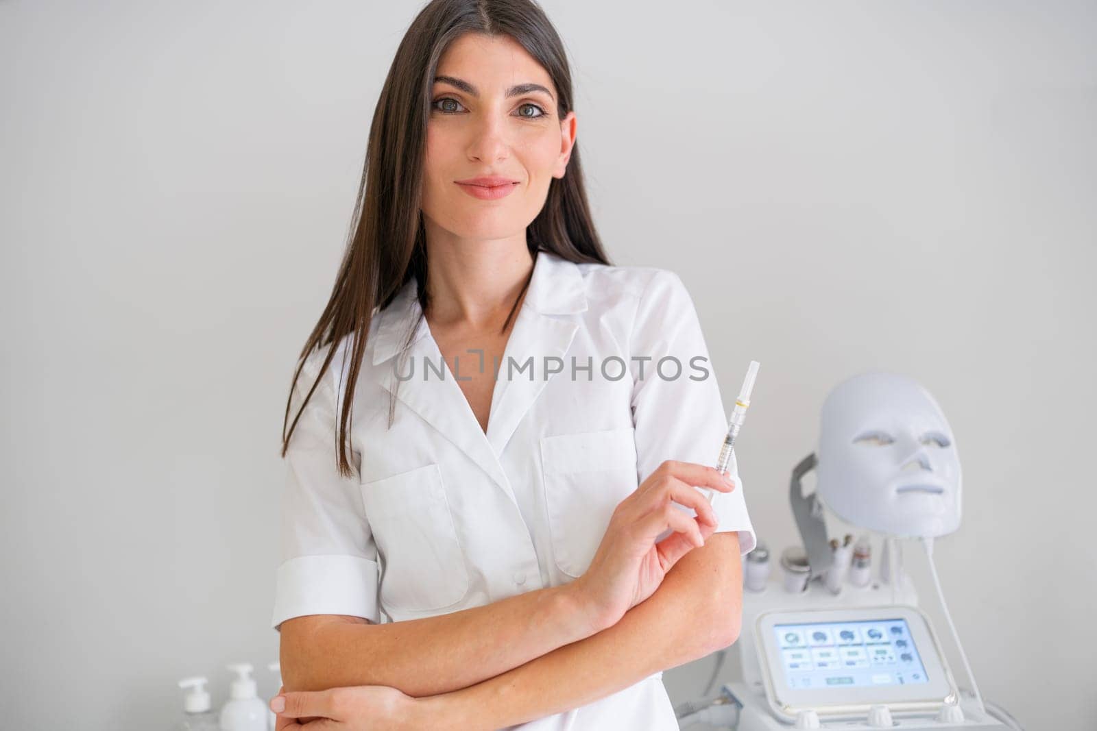 Woman cosmetologist standing hold injection syringe and looking at camera in beauty spa salon. Female dermatologist, skin therapist, beautician skincare professional in clean white coat uniform