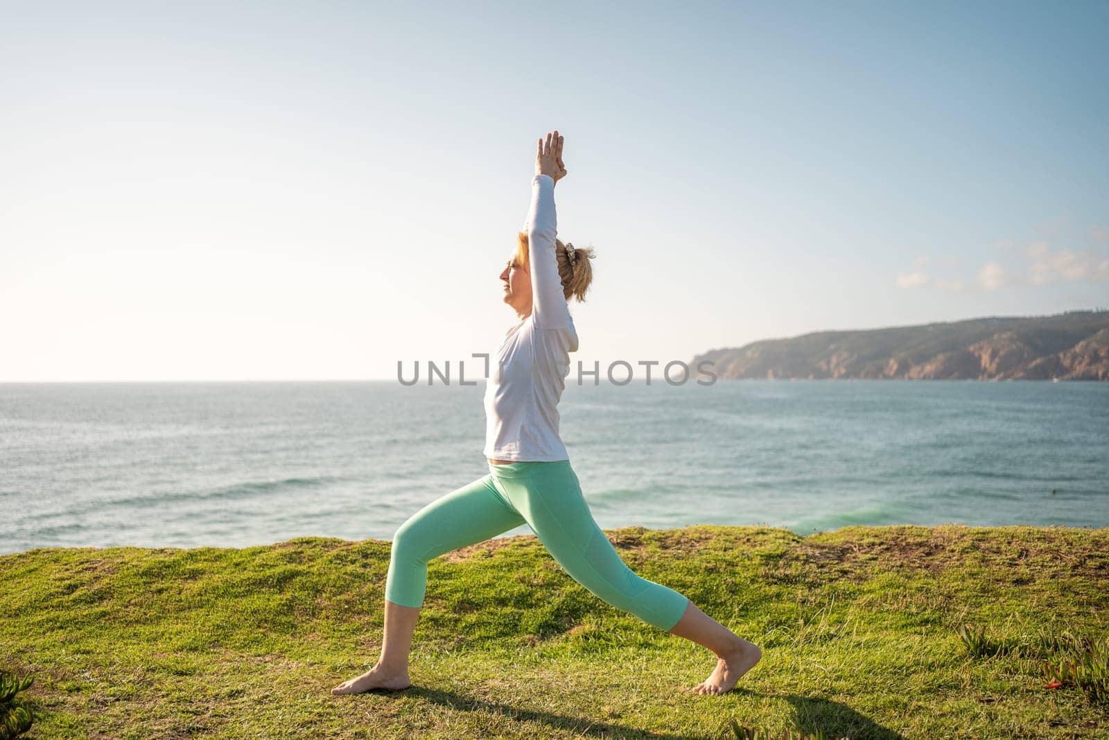 Elderly woman gracefully performs warrior pose, virabhadrasana, on beautiful beach. Practices yoga sunny morning, healthy lifestyle on nature. This serves as wonderful example fitness and wellness.