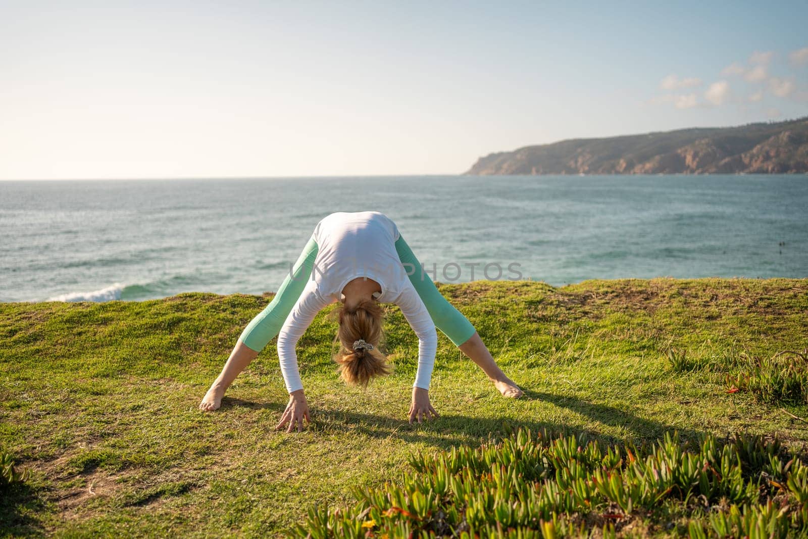 Senior woman doing yoga pose on ocean shore. Retired female practicing yoga and flexibility. Sports activities in nature. Wellness concept, yoga exercise