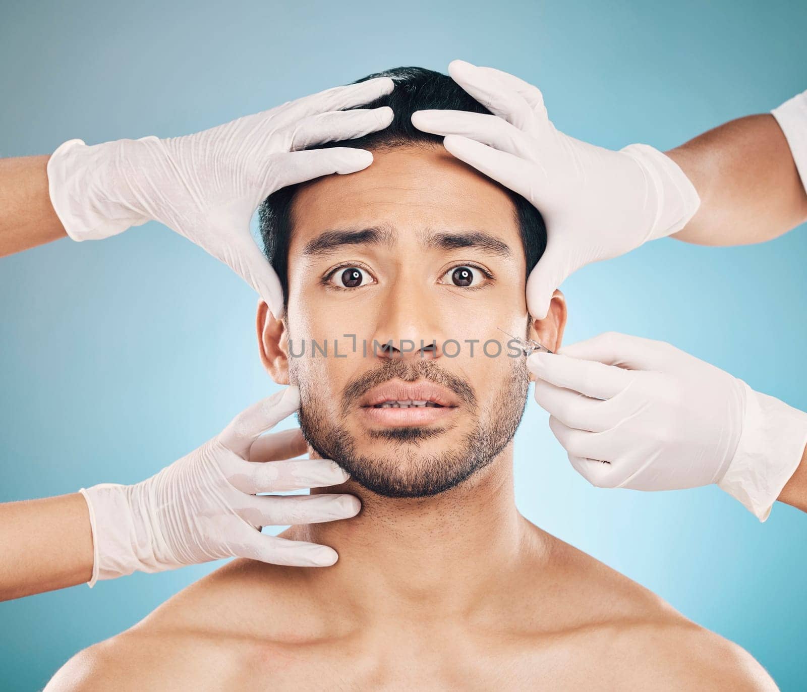 Portrait, hands and plastic surgery with a nervous man in studio on a blue background for beauty enhancement. Face, botox and change with a young male patient looking worried in a clinic for skincare.