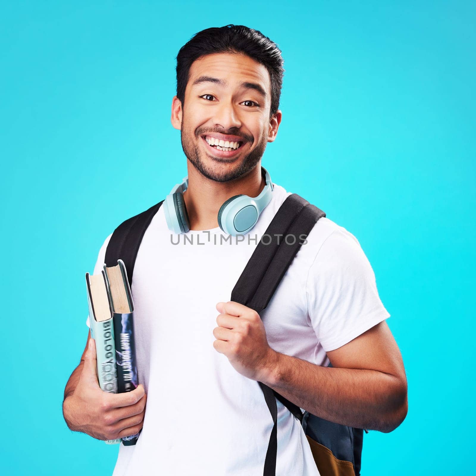 Indian, college student and portrait in studio with backpack for university, education and studying with books on blue background. Happy, man and person excited to study and learn for future goals.