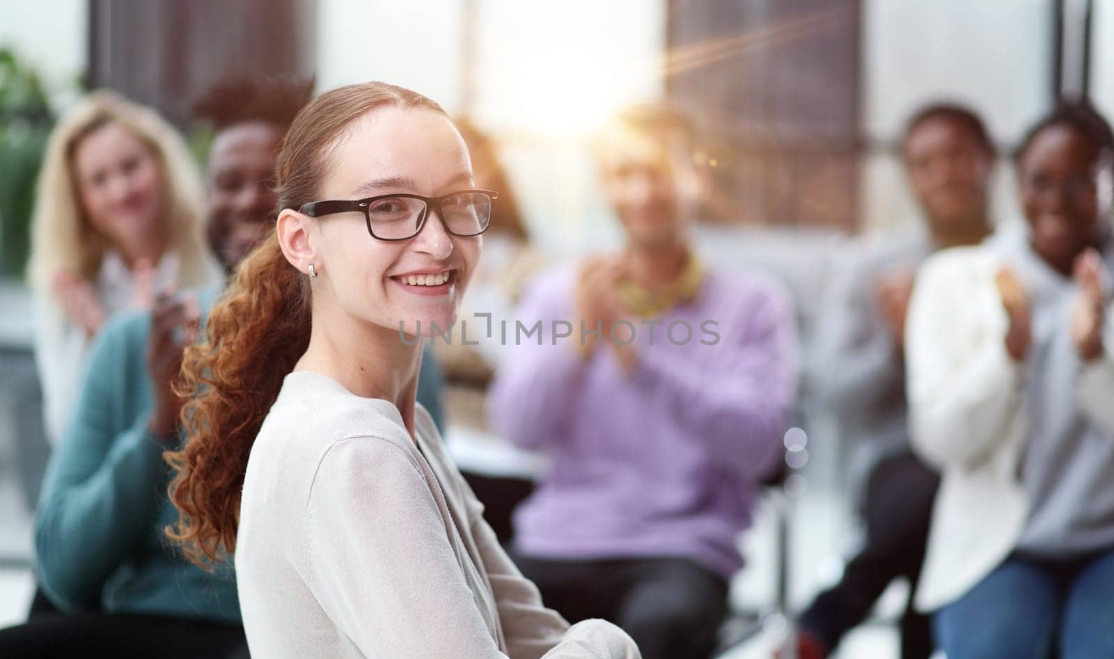 Smiling businesswoman in glasses looking at camera at a seminar with her colleagues nearby