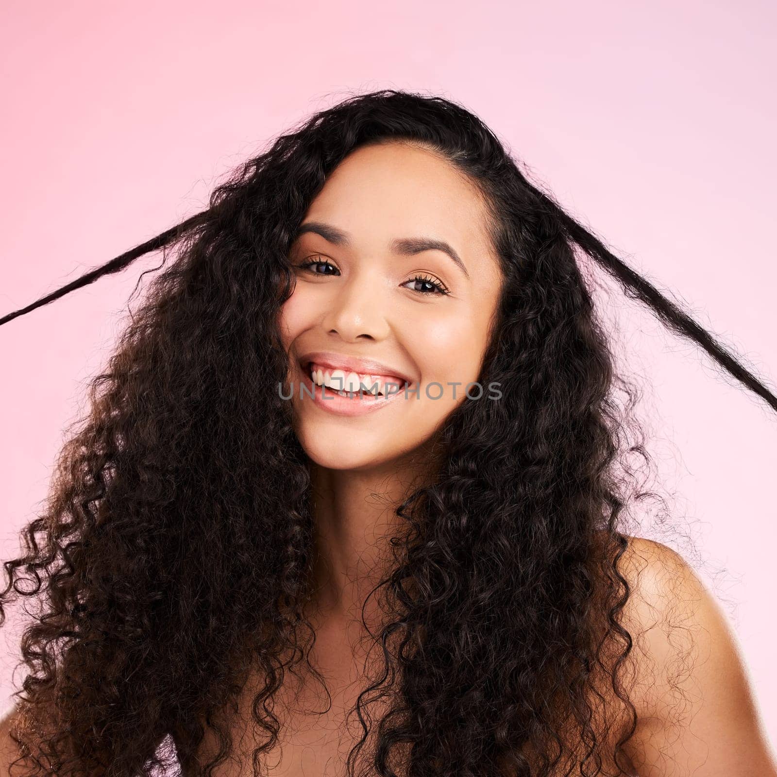 Face, woman and curly hair pull for beauty in studio isolated on a pink background. Portrait, natural cosmetics and hairstyle of happy model in salon treatment for growth, wellness and aesthetic.