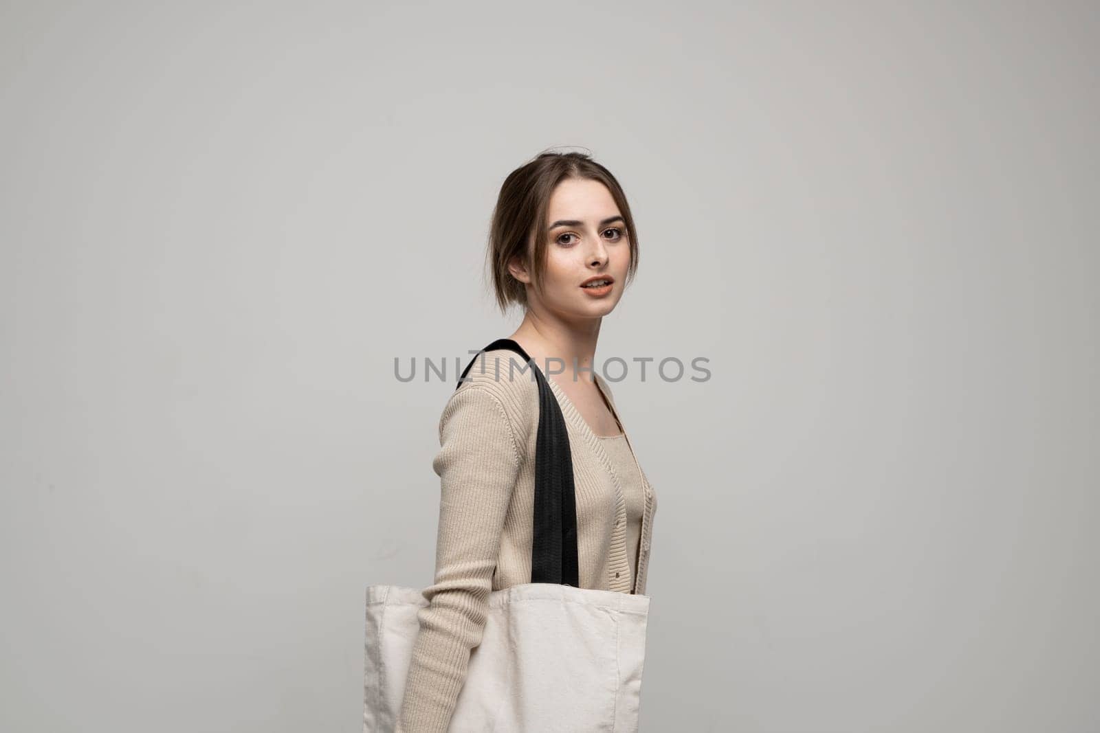 Cheerful millennial woman with a white eco bag standing over white studio background. Lady holding shopper handbag. Fashion and ecology concept, Selective Focus. No more plastic. by vovsht