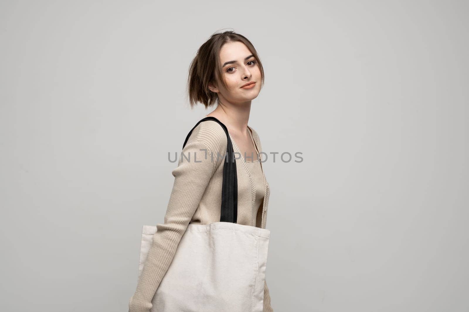 Young brunette woman in a casual beige clothes with cotton shopping bag on a shoulder. Eco friendly lifestyle. Isolated white background