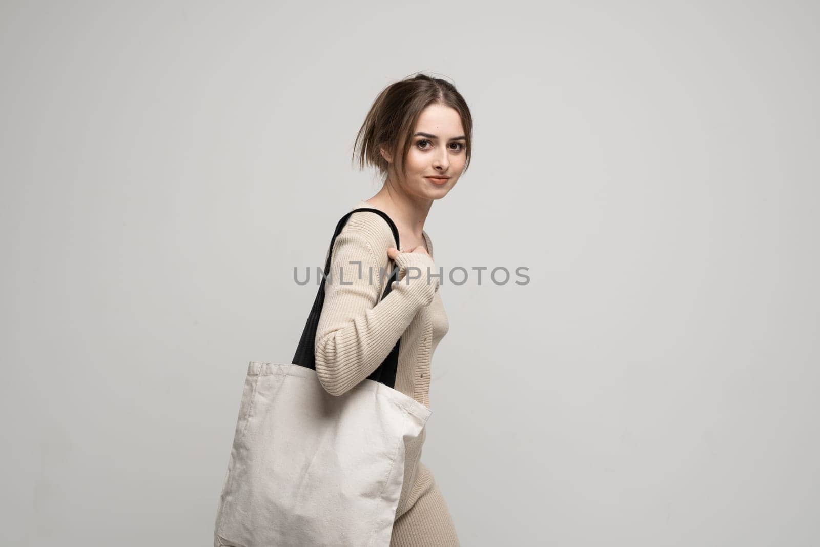 Cheerful happy woman in a beige costume with white cotton bag in her hands. Mockup and zero waste concept. Eco friendly lifestyle. Reuse, recylce, zero waste, No more plastic. by vovsht