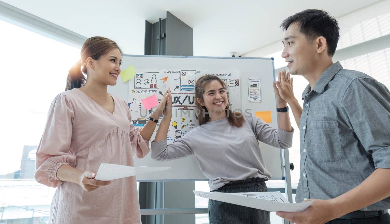 Asian female leader and ux ui designer clapping hand for successful of mobile app interface wireframe design at modern office. Creative digital development agency.