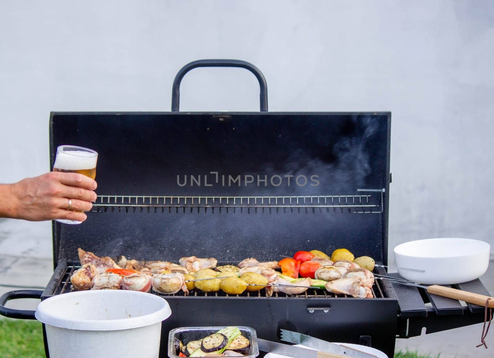 men hold beer in their hands on the background of the grill, vegetables and meat. Selective focus. Nature