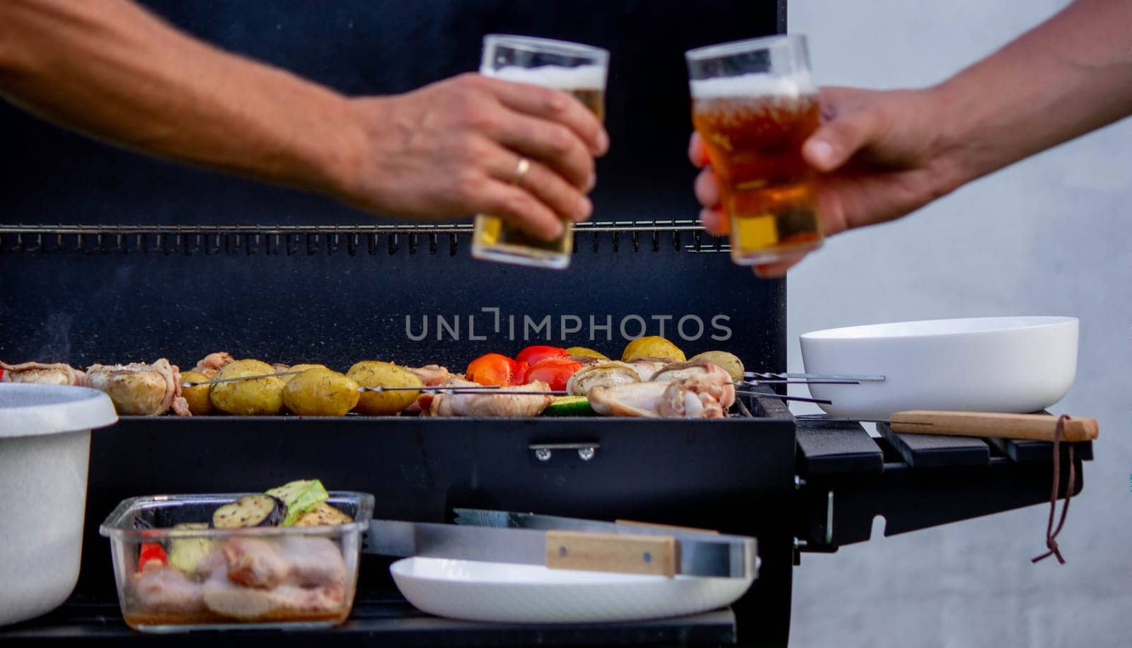 men hold beer in their hands on the background of the grill, vegetables and meat. Selective focus. Nature
