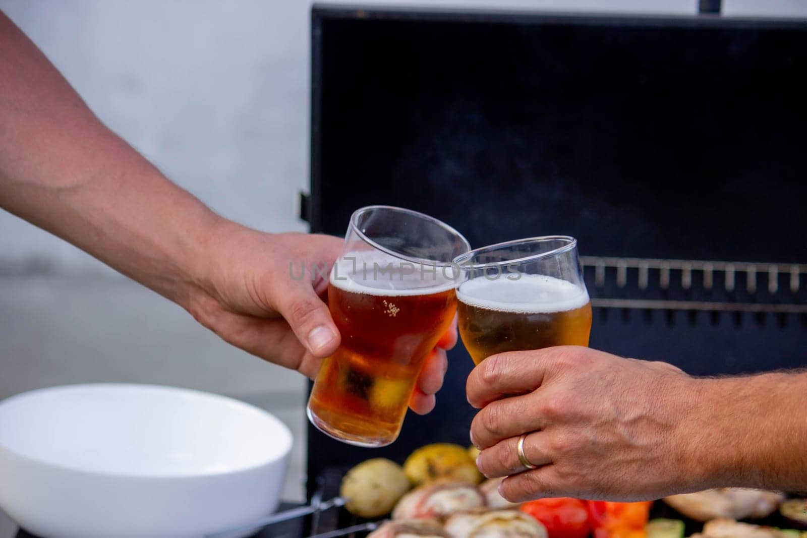 men hold beer in their hands on the background of the grill, vegetables and meat. Selective focus. Nature