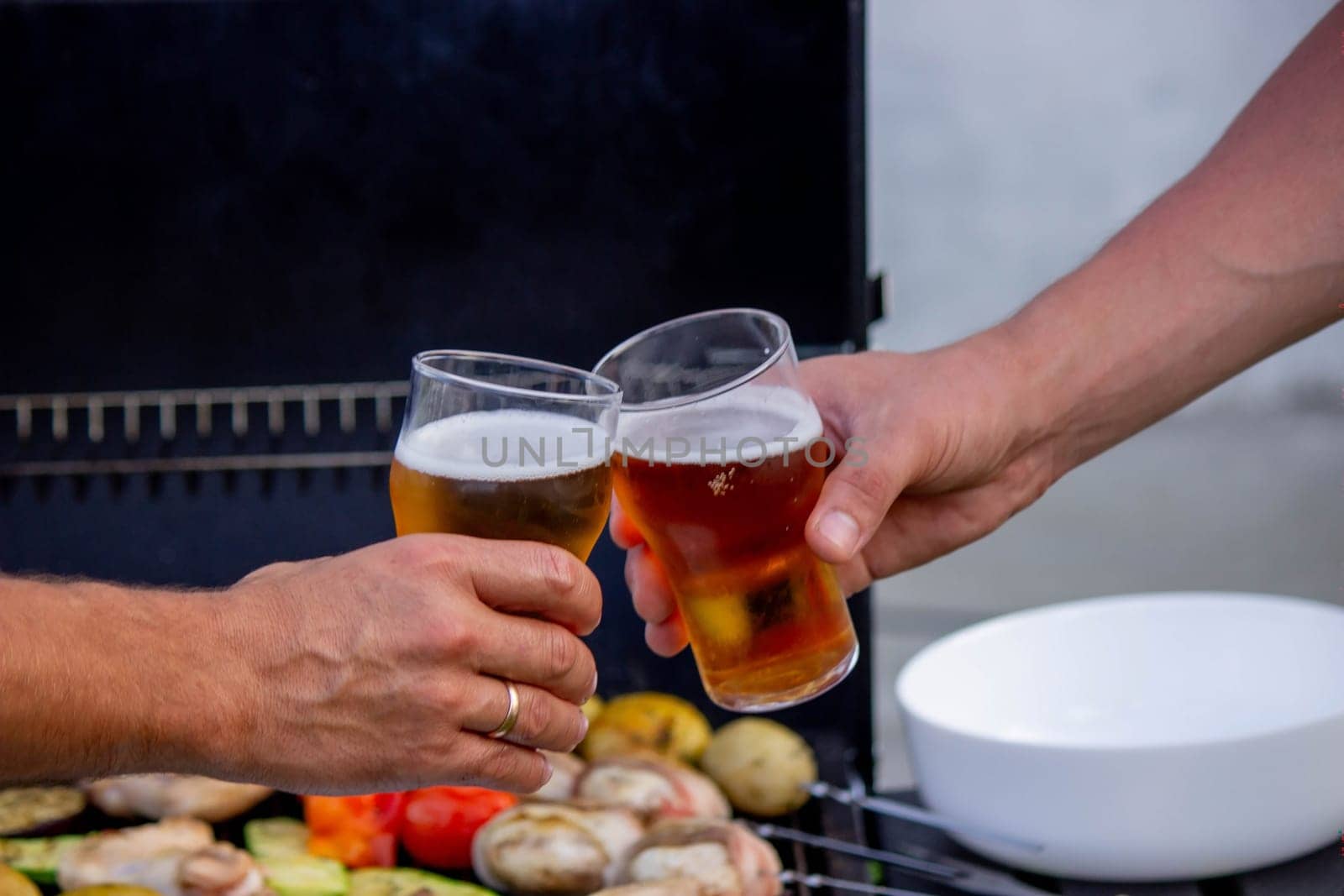 men hold beer in their hands on the background of the grill, vegetables and meat. Selective focus. Nature