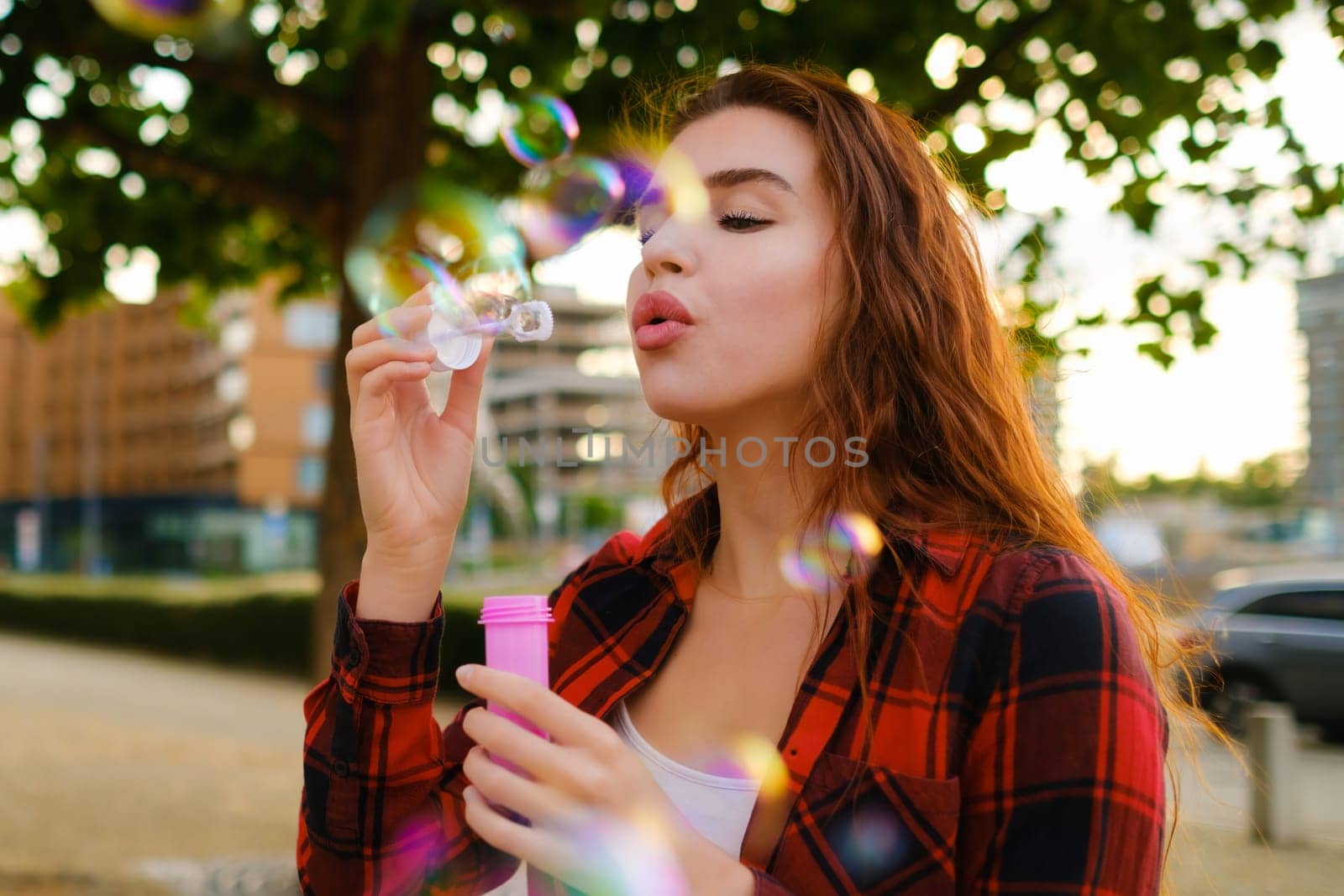 Red haired girl in a red plain shirt blowing air bubbles standing in the street.