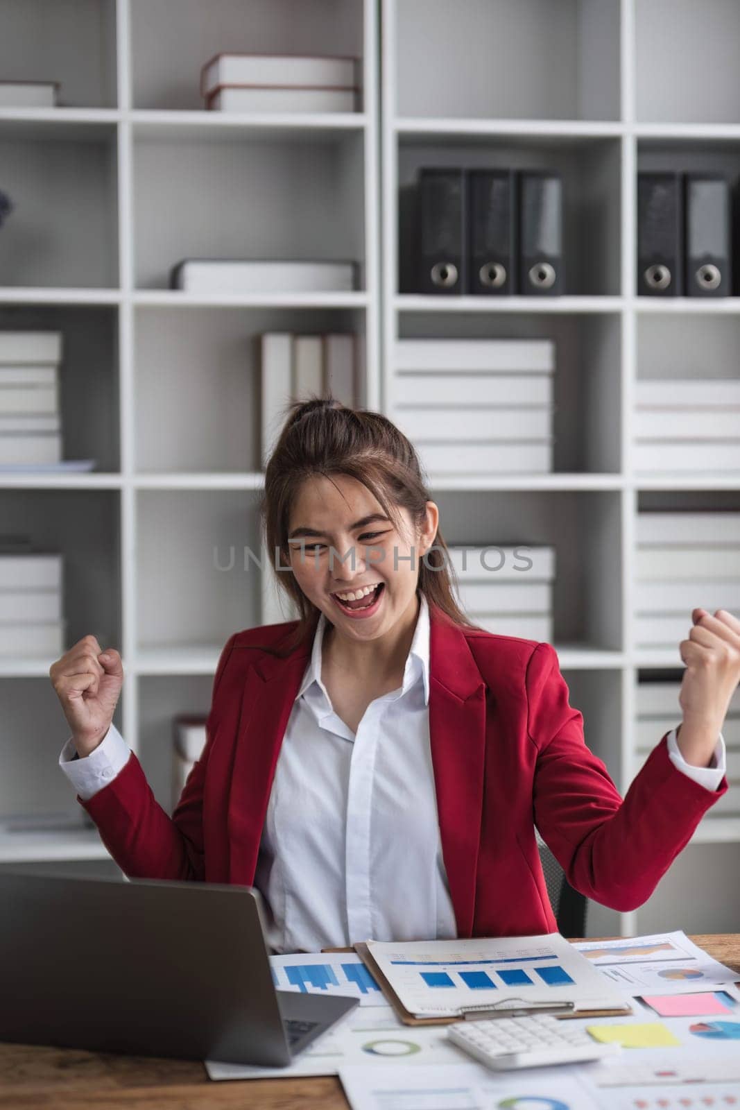 Beautiful Asian businesswoman celebrate while using laptop at office and showing delight. Startup small business and successful concept by wichayada