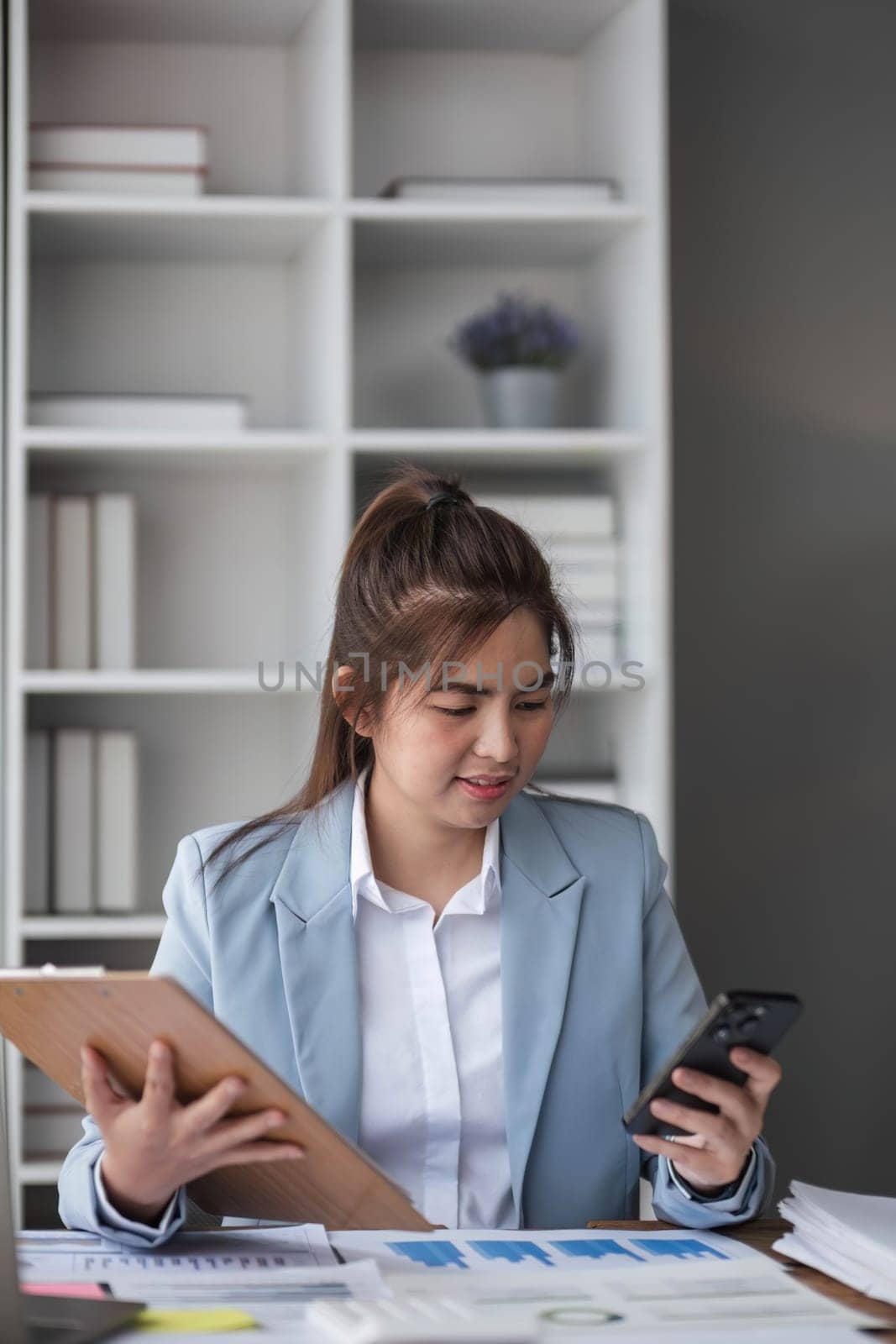 Portrait of young business woman with sitting in office in front of her laptop and talking on mobile phone hand at office.