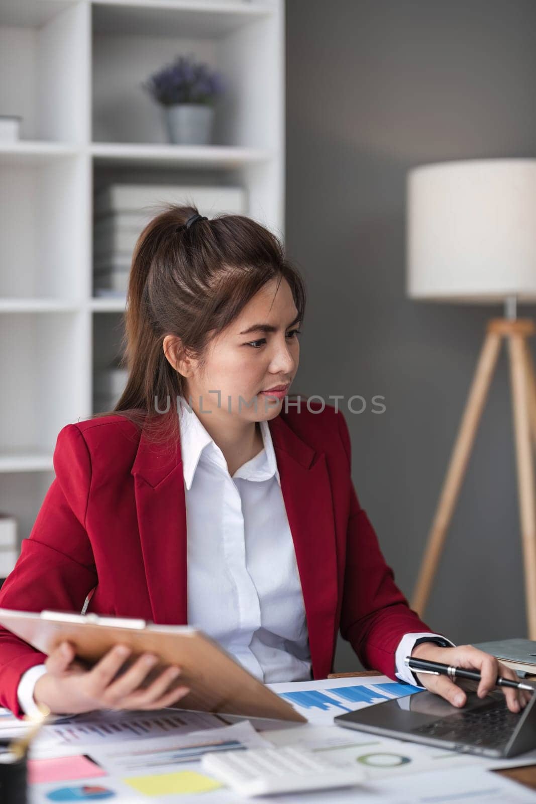 Cheerful business lady working on laptop in office, Asian happy beautiful businesswoman in formal suit work in workplace. Attractive female employee office worker smile by wichayada