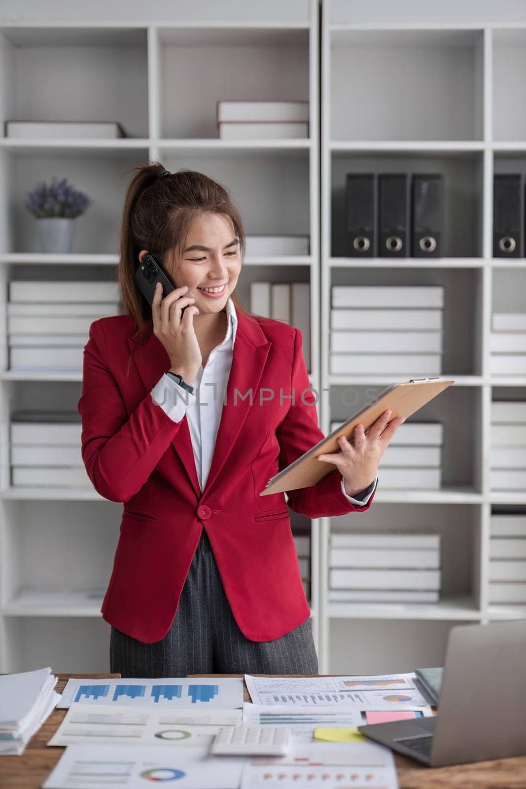 Portrait of young business woman with standing in office in front of her laptop and talking on mobile phone hand at office.