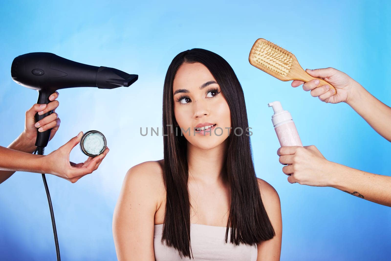 Hair care, beauty and tools with a woman in studio with a hairdryer, self care product and brush. Salon, hairdresser and a female model person thinking of shampoo and cosmetics on a blue background by YuriArcurs
