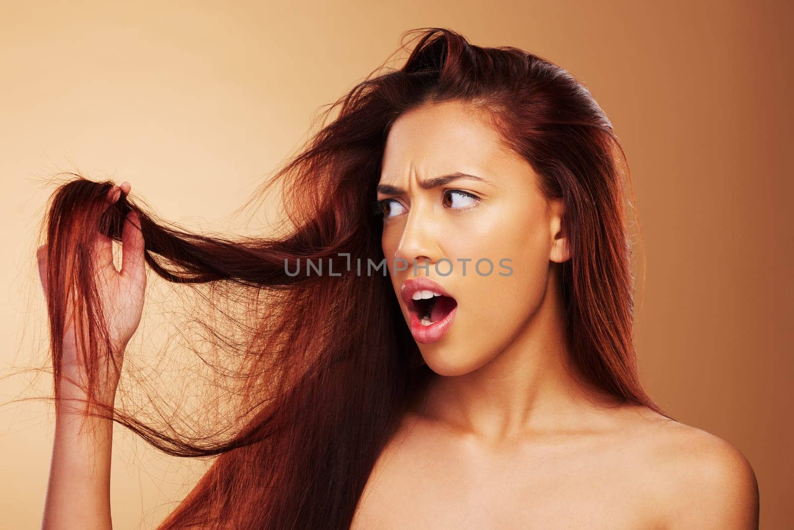 Damaged, hair and a woman upset in studio about salon, split end and hairdresser treatment. Stress, disaster and shocked model person with dry texture or hairstyle crisis on a brown background.