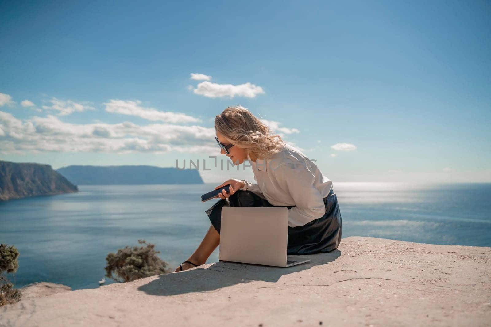 Freelance women sea working on a computer. Pretty middle aged woman with computer and phone outdoors with beautiful sea view. The concept of remote work. by Matiunina