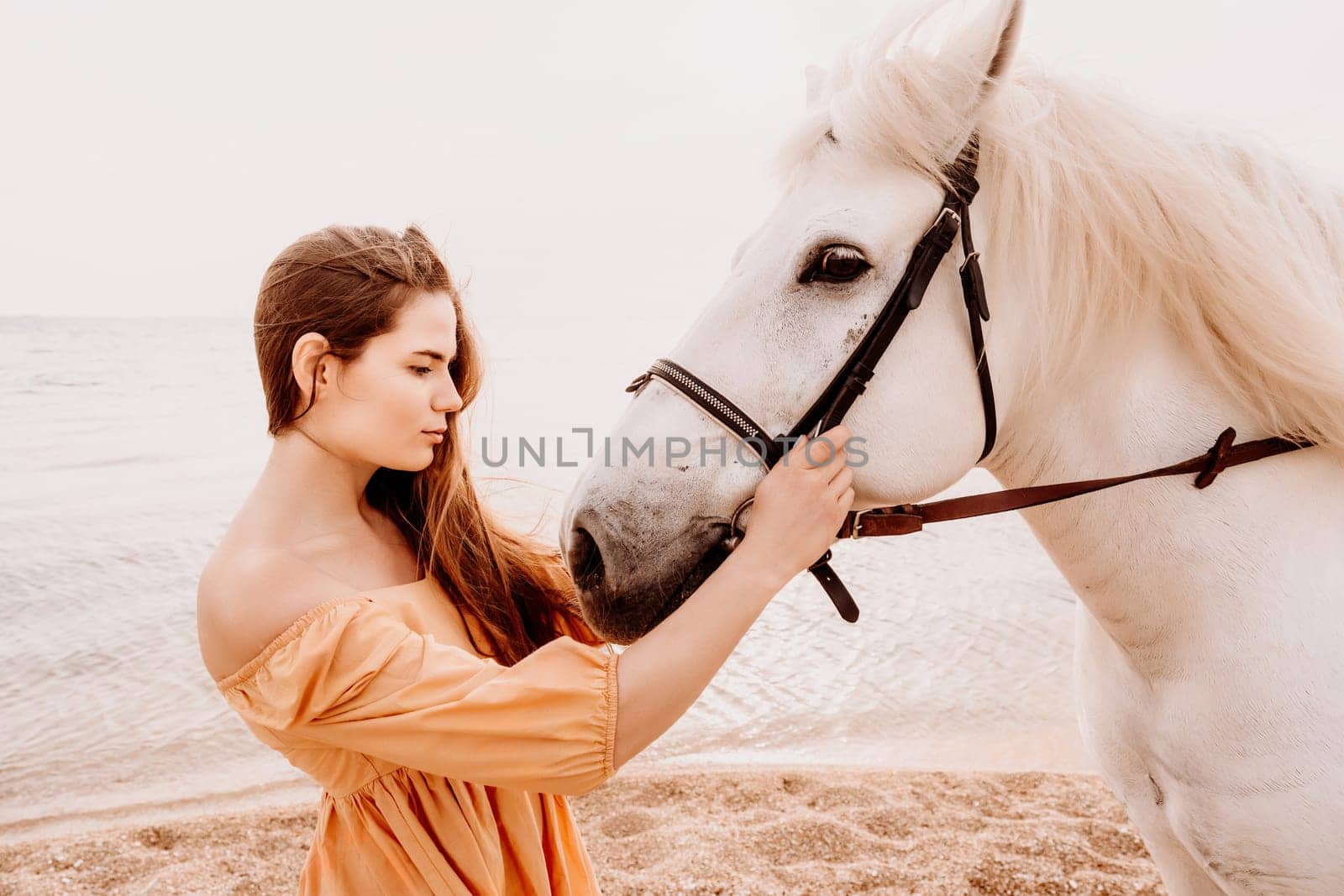 A woman in a dress stands next to a white horse on a beach, with the blue sky and sea in the background