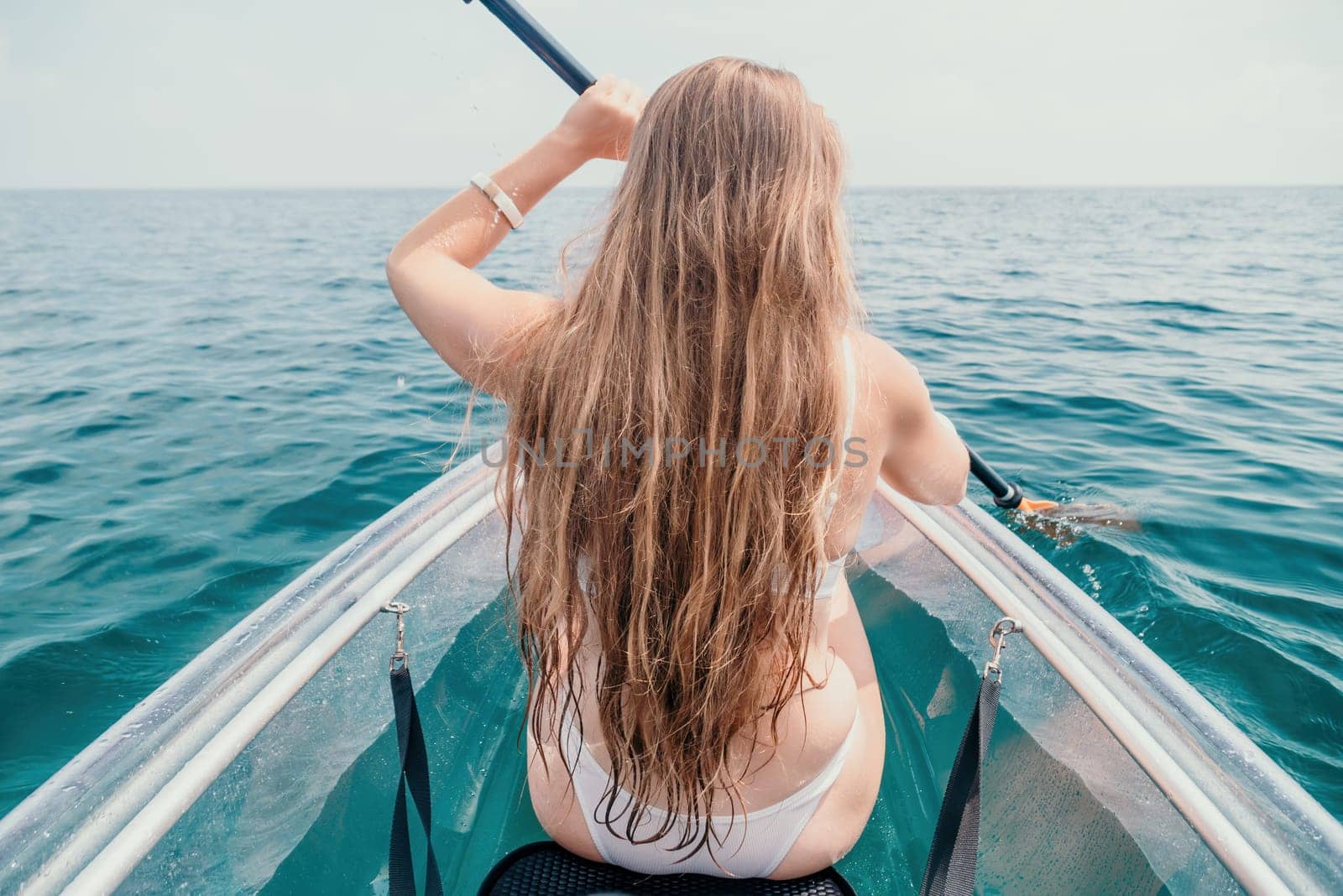 Woman in kayak back view. Happy young woman with long hair floating in transparent kayak on the crystal clear sea. Summer holiday vacation and cheerful female people relaxing having fun on the boat by panophotograph