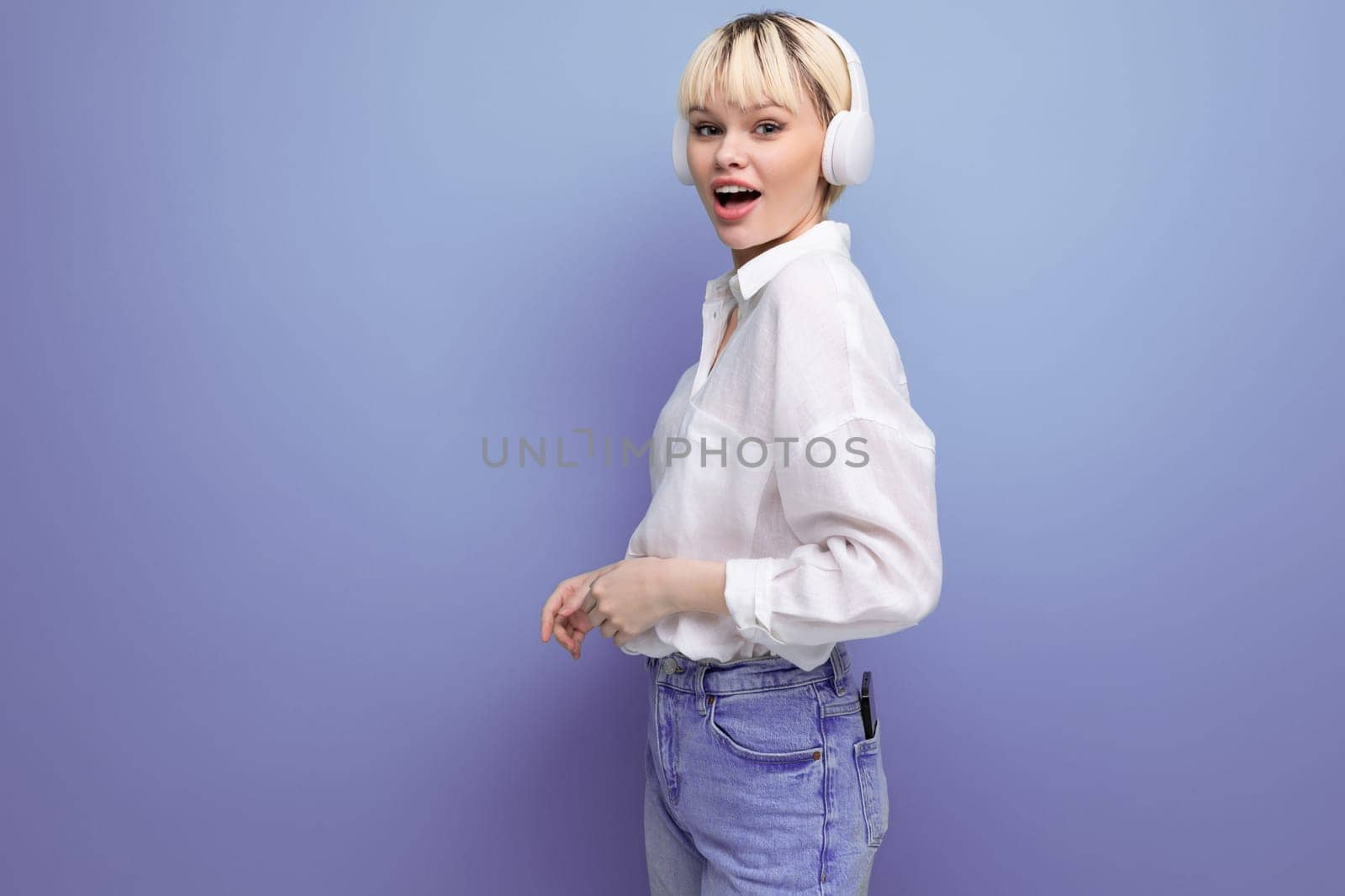 young successful pretty blond office worker woman in a white shirt and jeans uses headphones during a break. business concept.