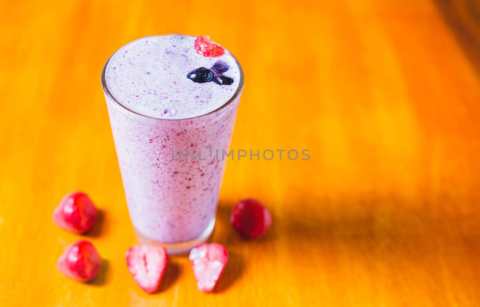 Strawberry milkshake on wooden table. Strawberry smoothie with blueberry on wooden background.  by isaiphoto